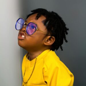 Adorable child in vibrant yellow attire and blue sunglasses, exuding style and confidence.