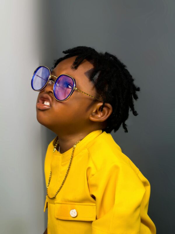 Adorable child in vibrant yellow attire and blue sunglasses, exuding style and confidence.