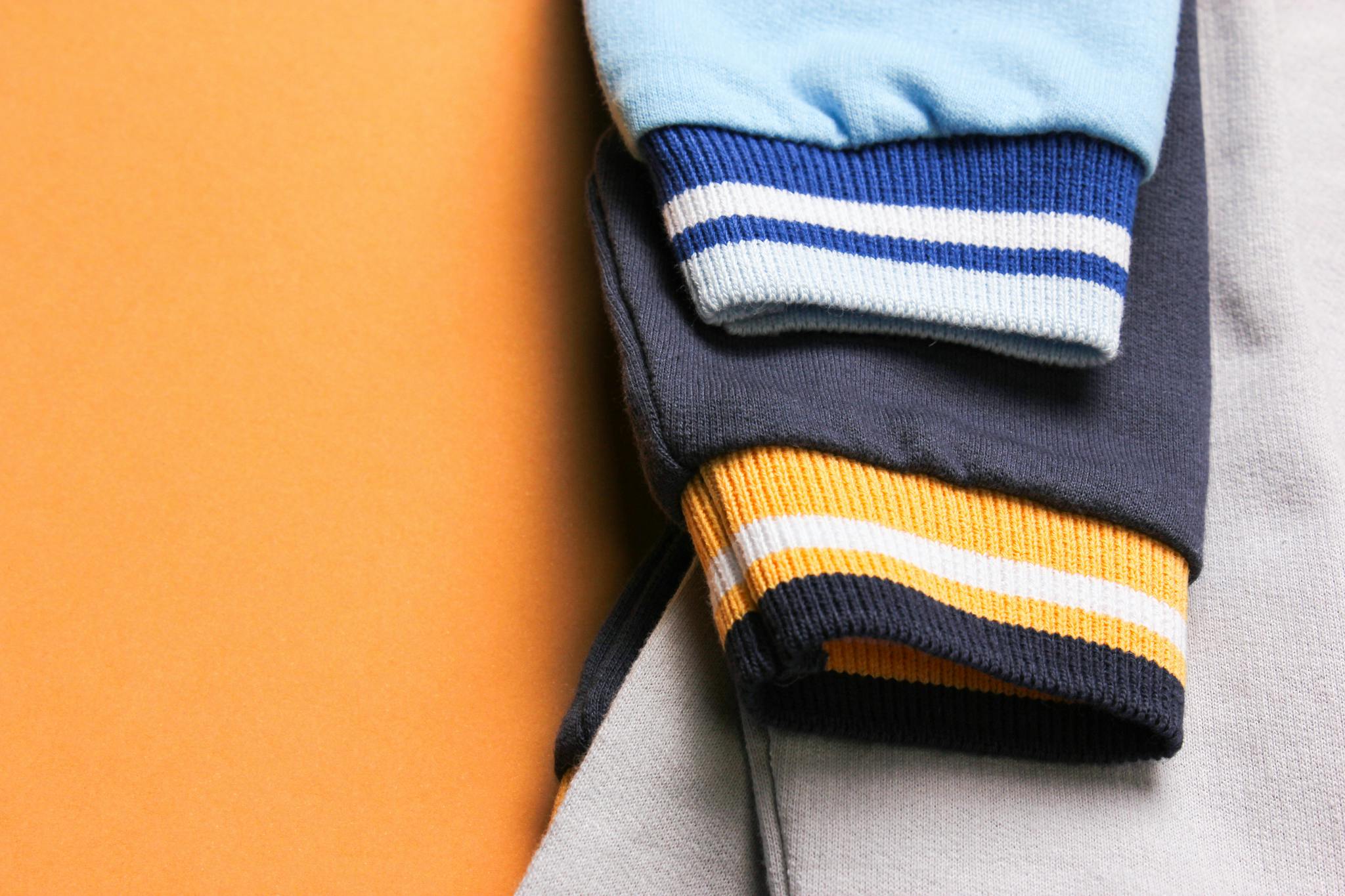 Close-up of vibrant baby fashion outfit with striped cuffs on a bright orange background.